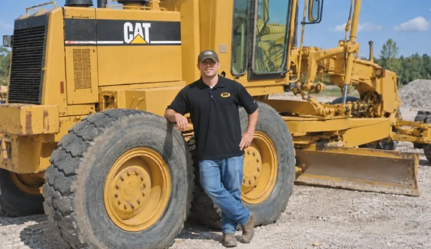 The appraiser standing beside a yellow Cat motor grader